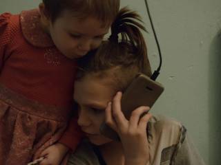 chlapec telefonuje, opírá se o něj menší dívka