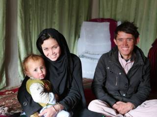 na zemi sedí muž a žena držící dítě, usmívají se