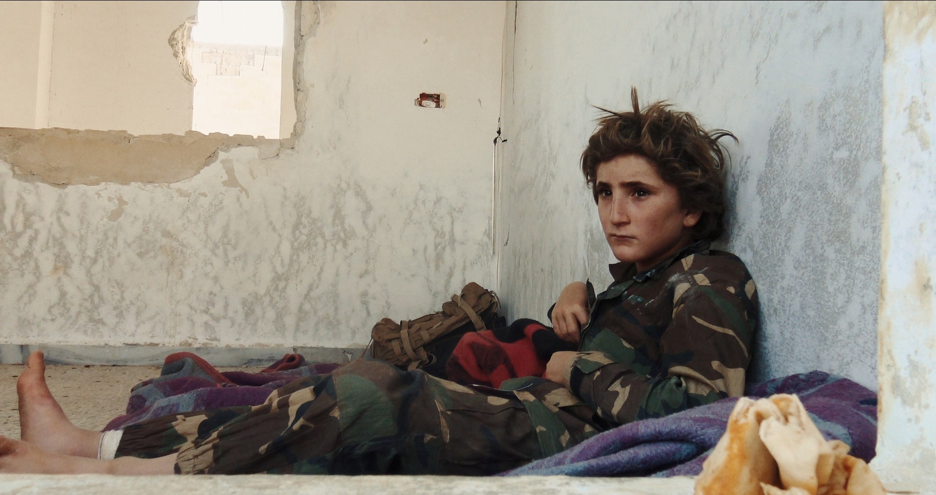 chlapec sedí na dece a opírá se o omšelou zeď