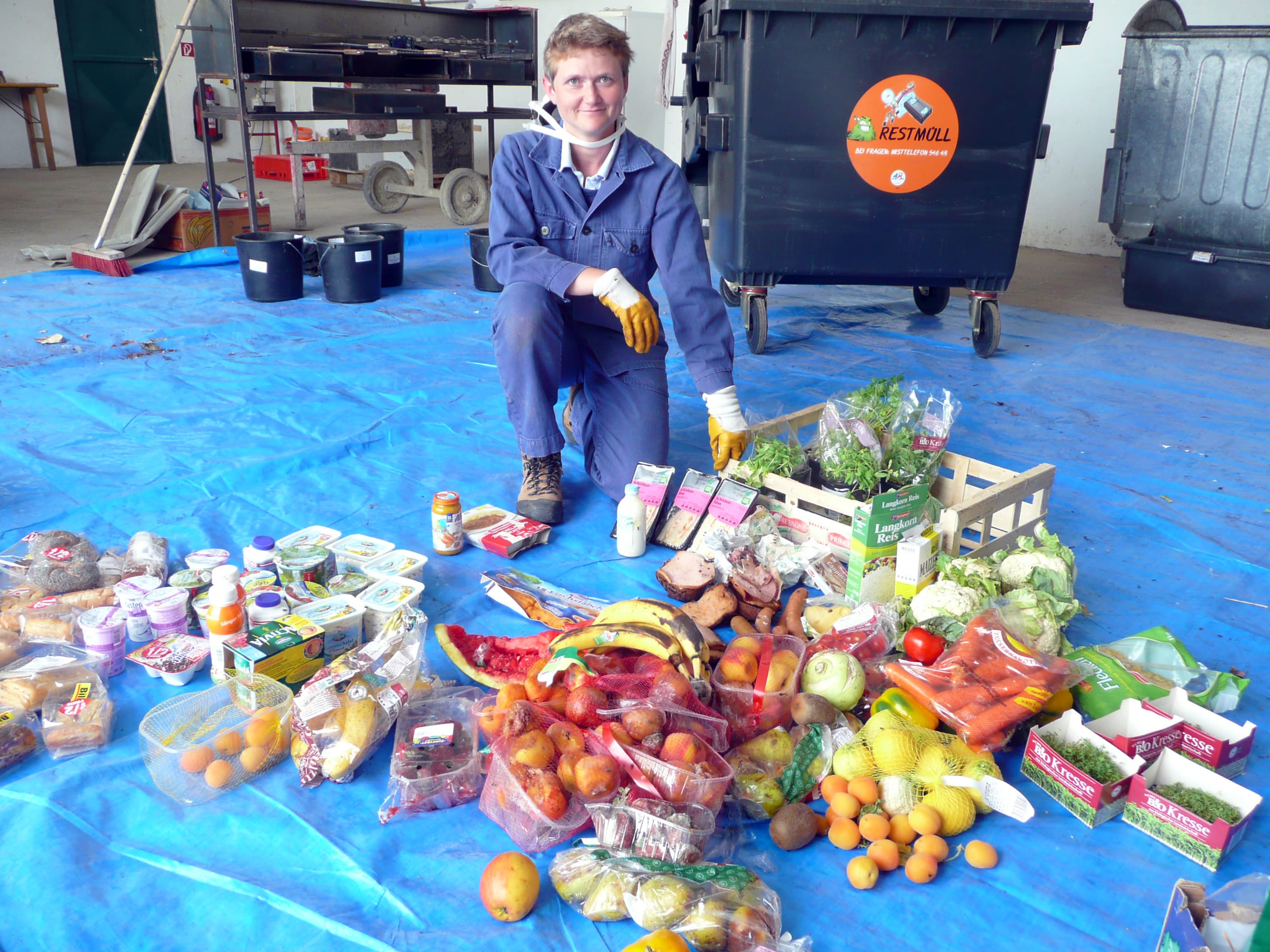 žena klečící nad velkým množství potravin zachráněných z popelnice